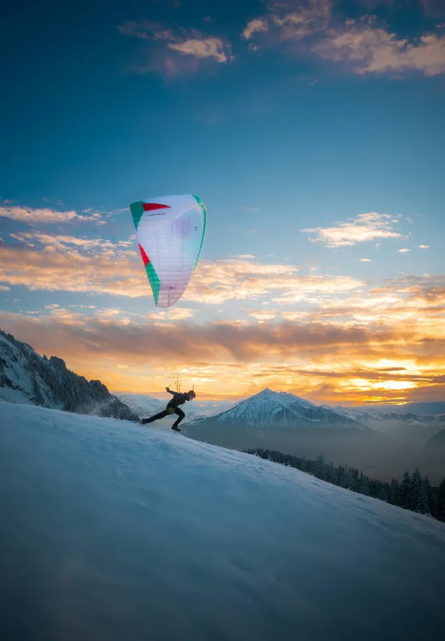 Launch: a paraglider takes off from a snowy slope at sunset